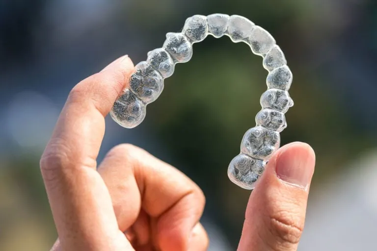 Hand holding a clear Invisalign aligner, showcasing orthodontic treatment options for teens and adults.