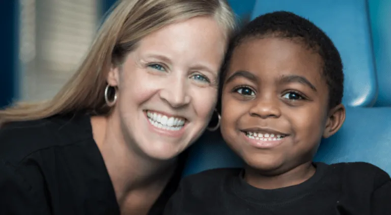 Dental hygienist and child smile together at pediatric dentist appointment.