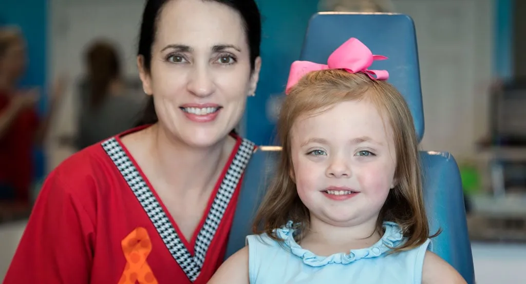 A child and a dental hygienist smiling during a pediatric dentistry appointment.