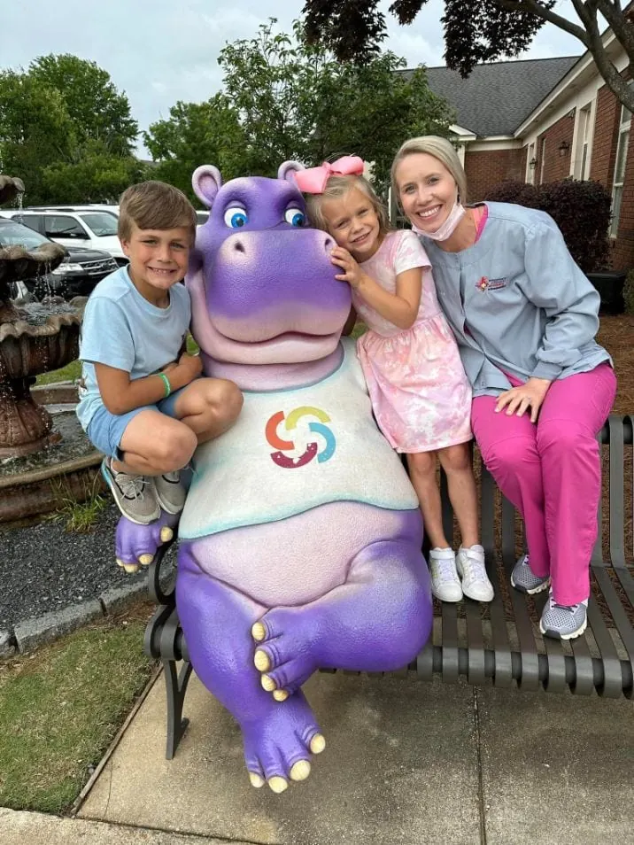 Dental hygienist and pediatric dentistry patients take photo with a hippo statue.