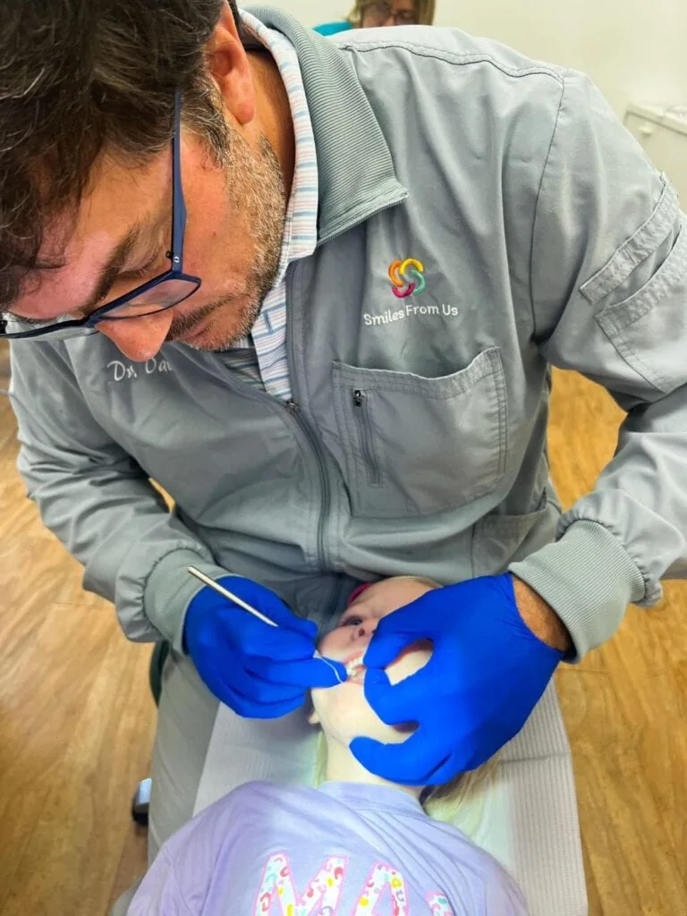 Dentist in gray coat examining child's mouth during dental check-up at pediatric dentistry office, emphasizing airway health and dental care.