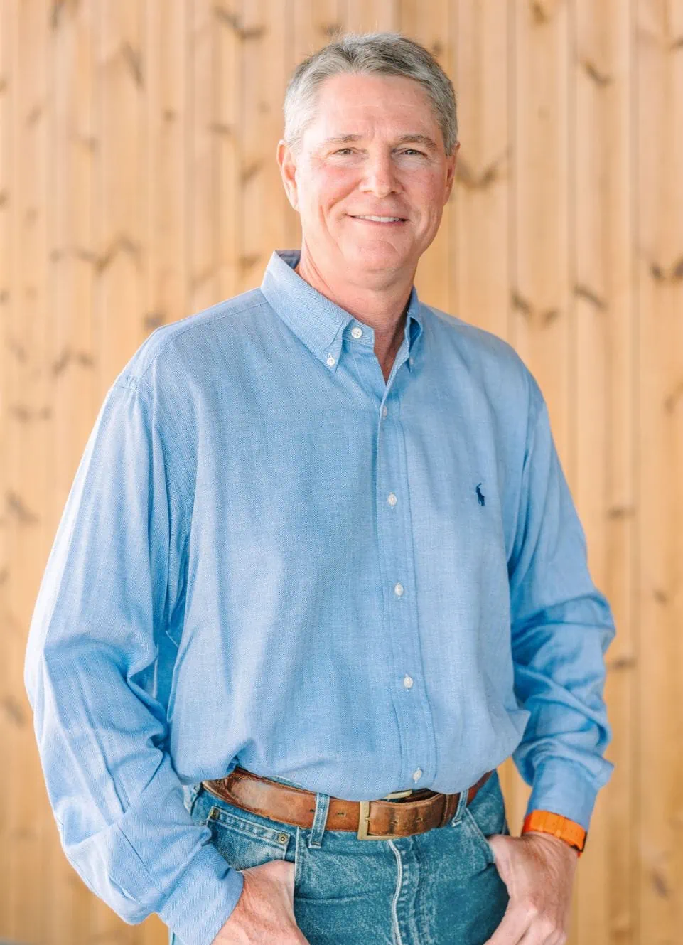 Dr. John Payne, pediatric dentist, smiling in a blue shirt against a wooden background, representing Montgomery Pediatric Dentistry.